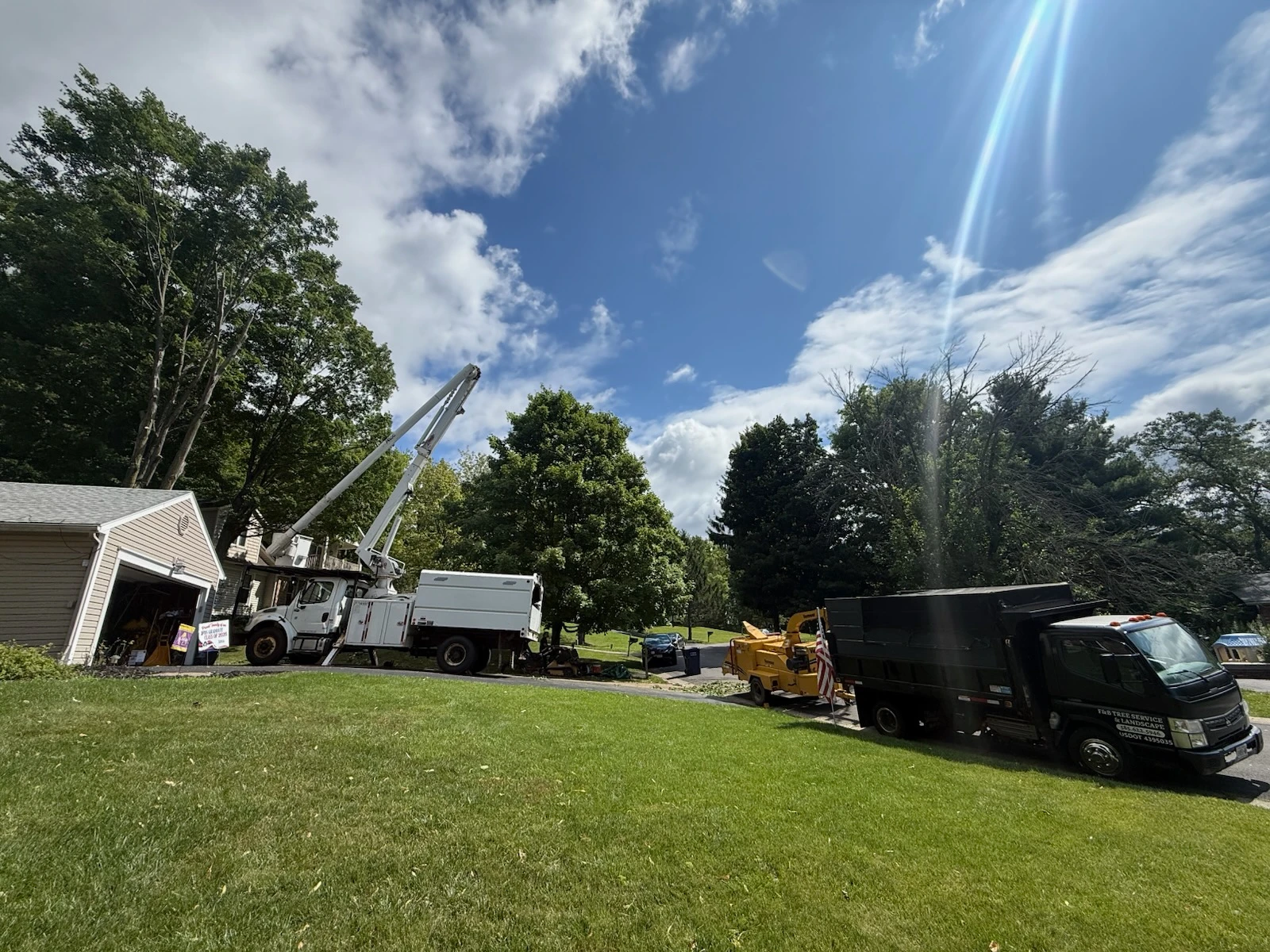 Bucket truck boom raised over a house while the F&B dump truck and chipper stage in the driveway