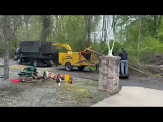 F&B crew feeding brush into the wood chipper beside the dump truck on a wooded driveway job
